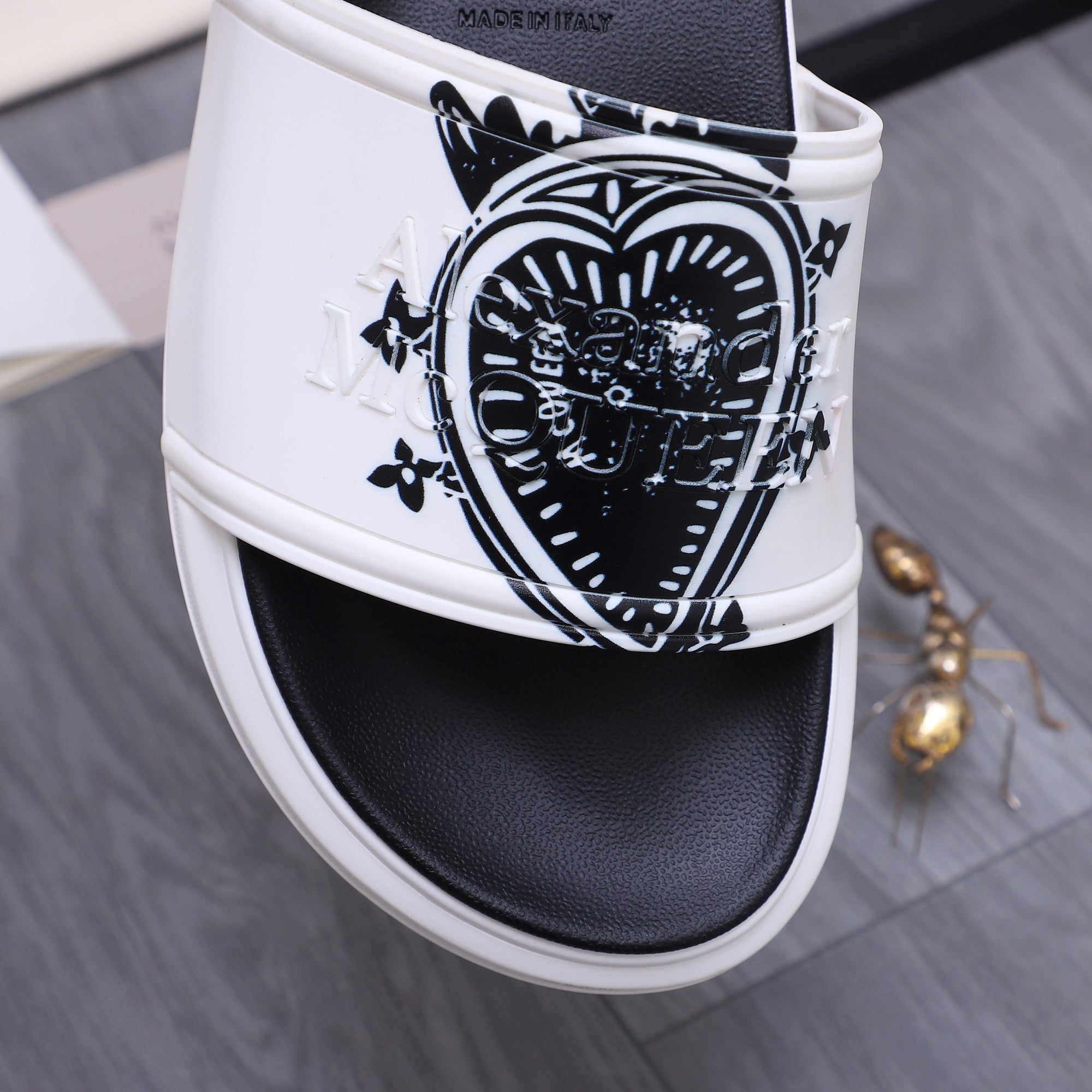 Alexander McQueen slide sandals, close-up of white strap with black crest graphic