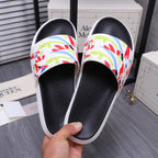 Black slide sandals with white rim and multicolor graffiti band, held for close view.