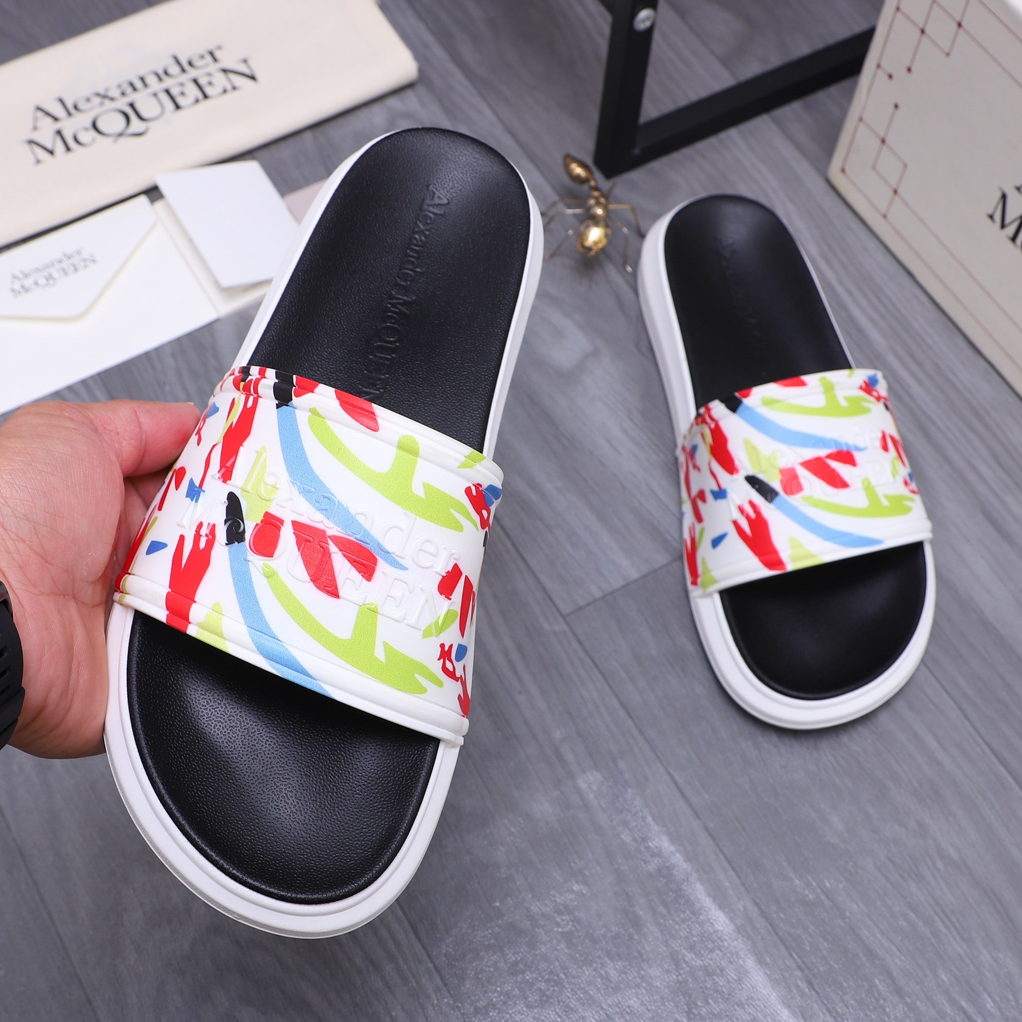 Black slide sandals on hand display, multicolor graffiti band and white sole.
