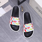 Two black slide sandals with multicolor graffiti band and white contrast soles.