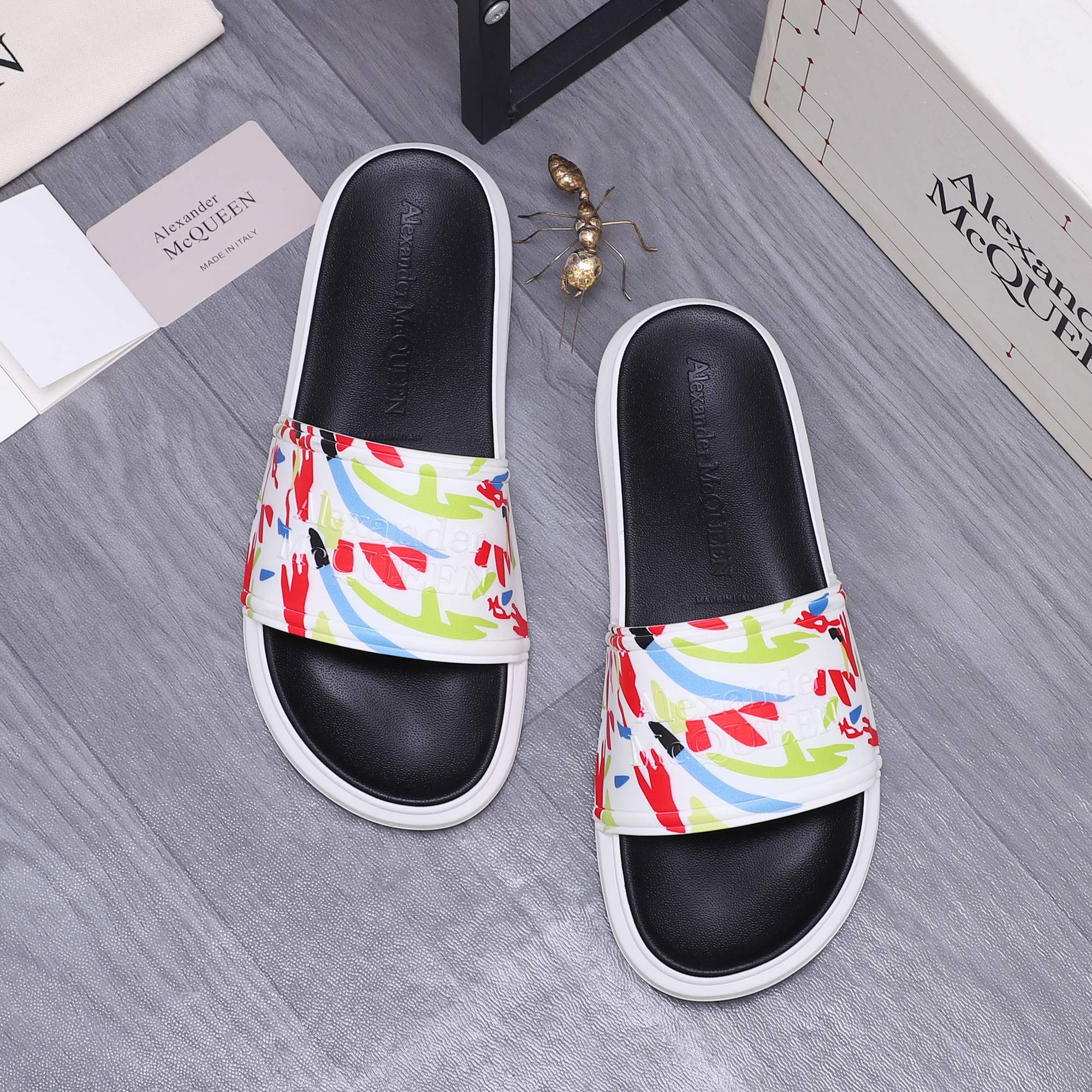 Two black slide sandals with multicolor graffiti band and white contrast soles.
