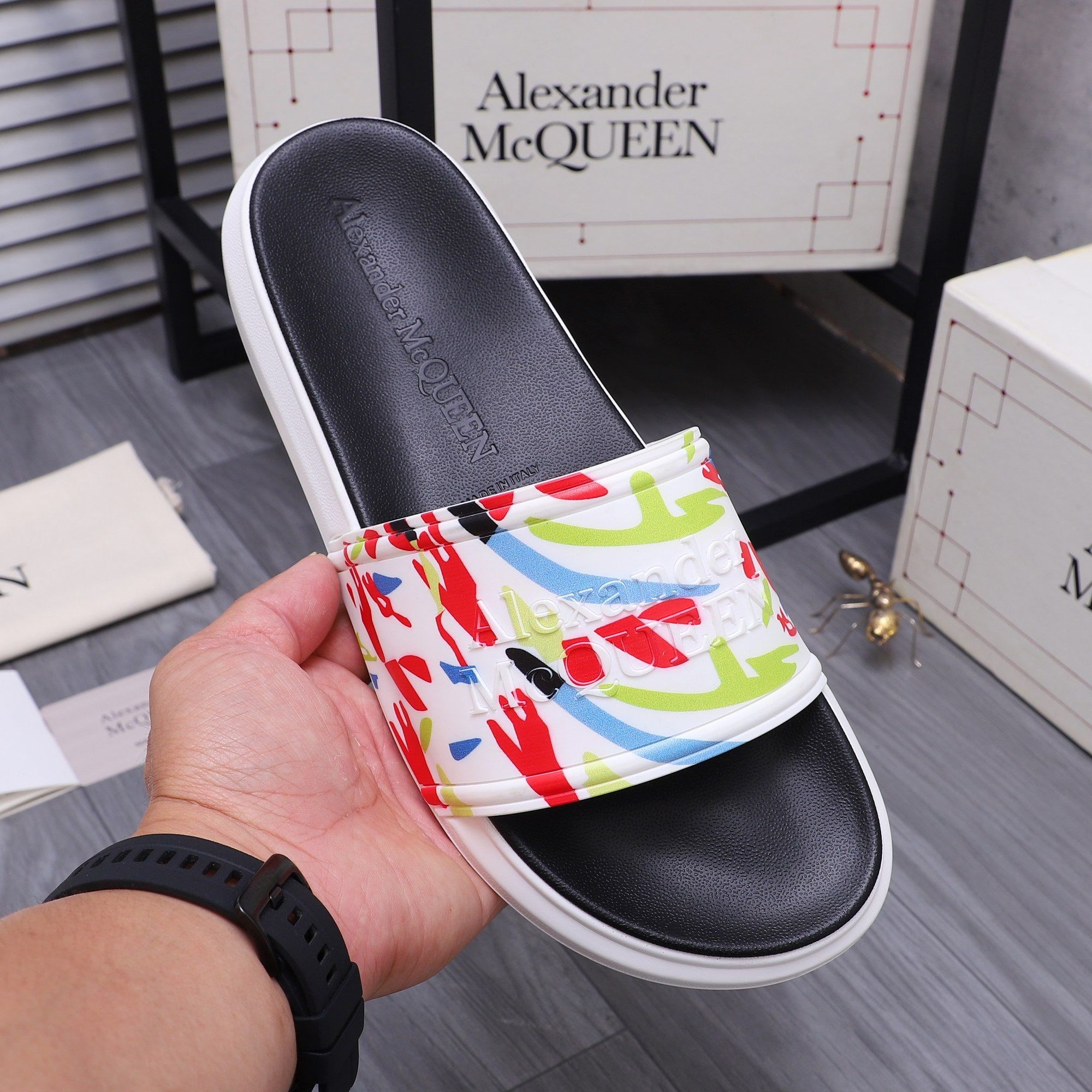 Black slide sandal on hand, multicolor graffiti upper band and white sole.