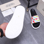 White outsole of slide sandal with black footbed and multicolor graffiti band.