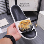 Alexander McQueen slide sandal, black footbed with white strap and gold print.