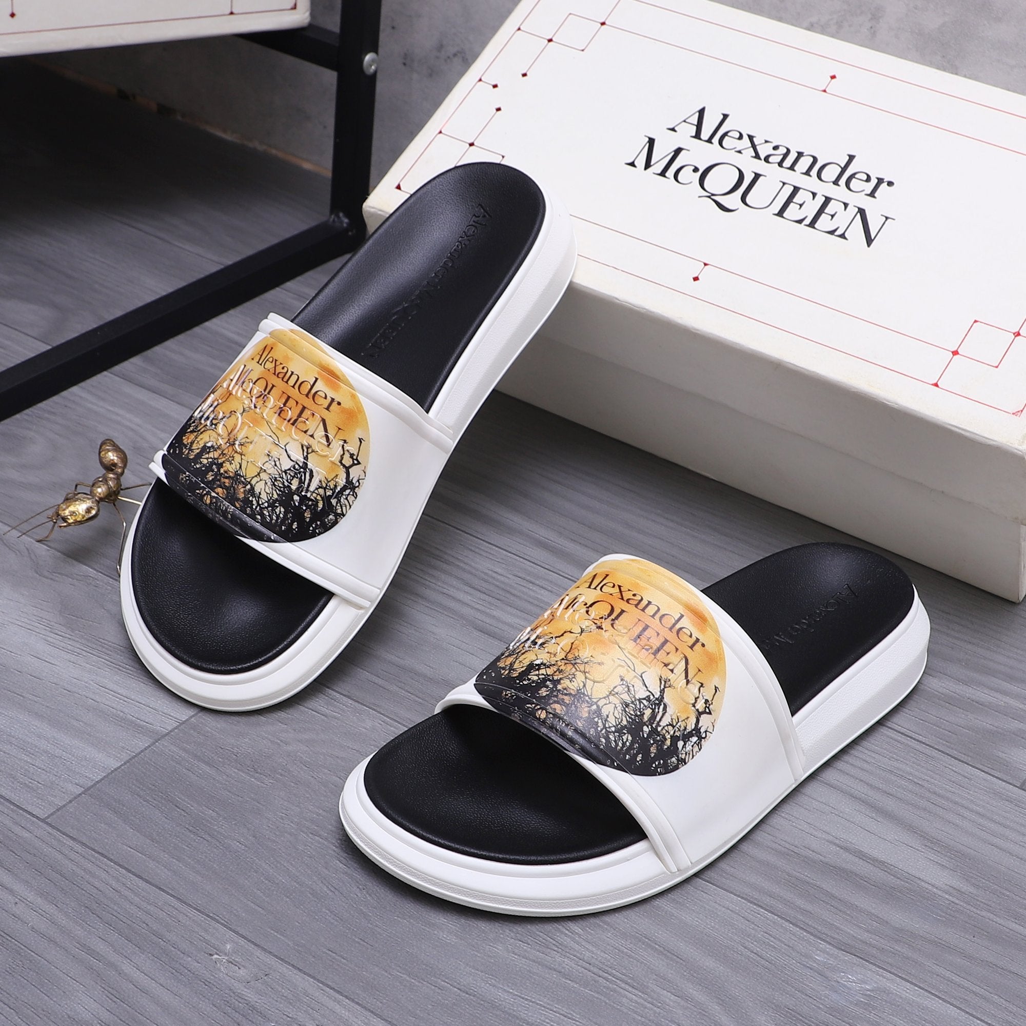 Alexander McQueen slide sandals, black footbeds, white straps, gold graphic print.