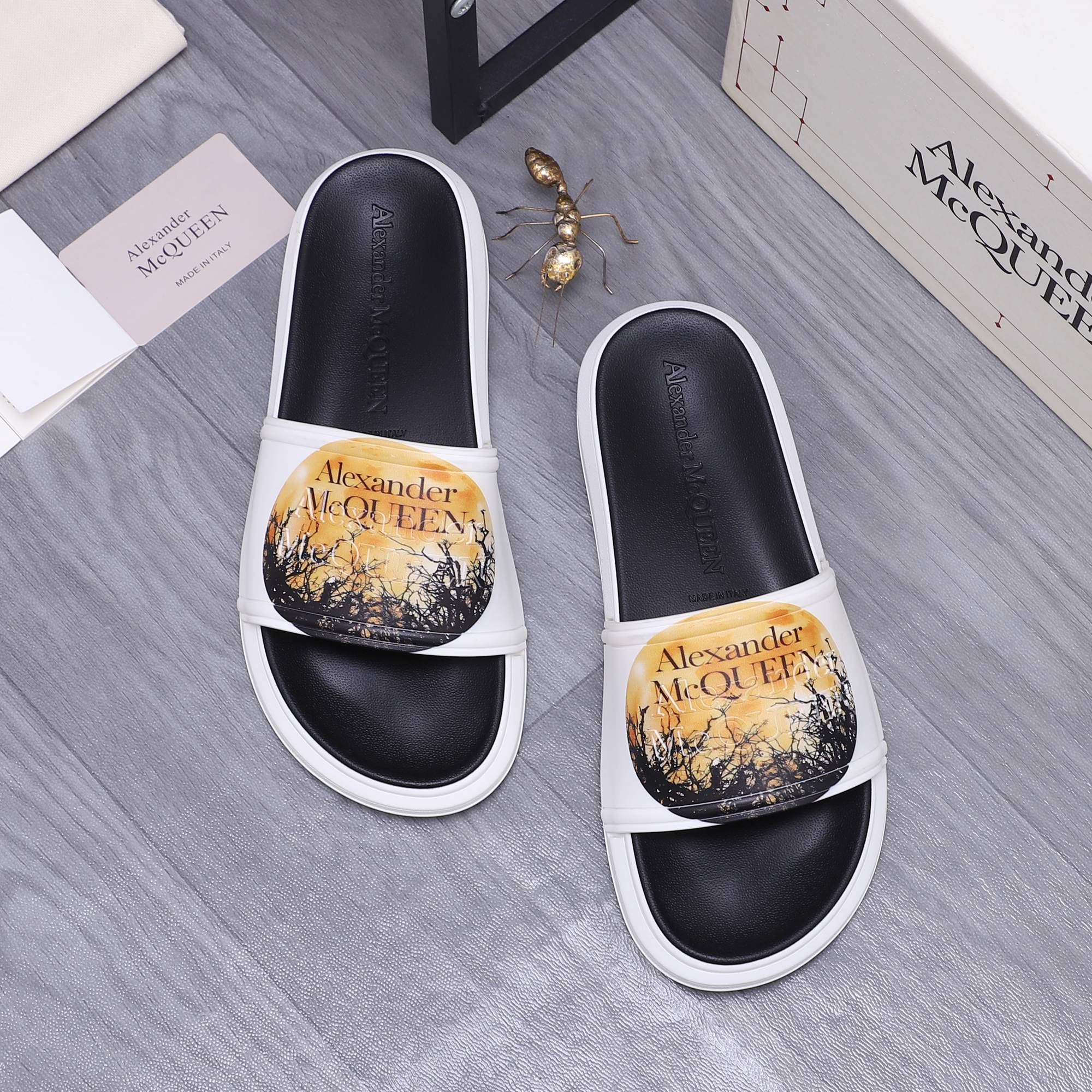 Alexander McQueen slide sandals with white straps and black footbeds, gold print.