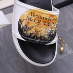 Alexander McQueen slide sandal close-up: white strap with gold graphic over black.