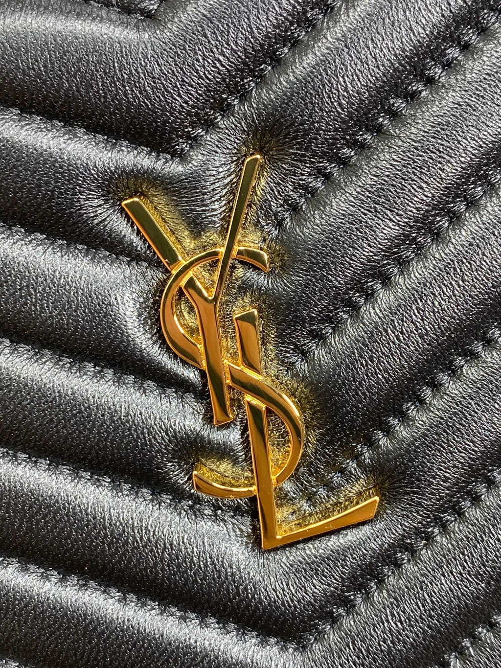 Gold YSL logo plaque on dark quilted leather with chevron stitched pattern
