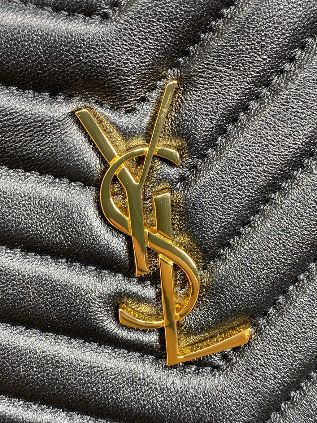 Close-up of gold YSL logo on dark blue quilted bag