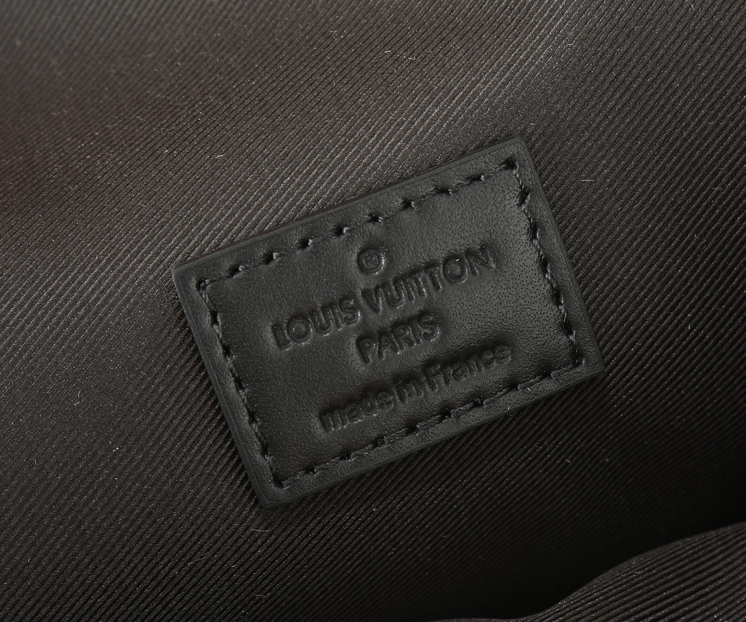 Louis Vuitton leather brand patch close-up on dark strap with stitched edges