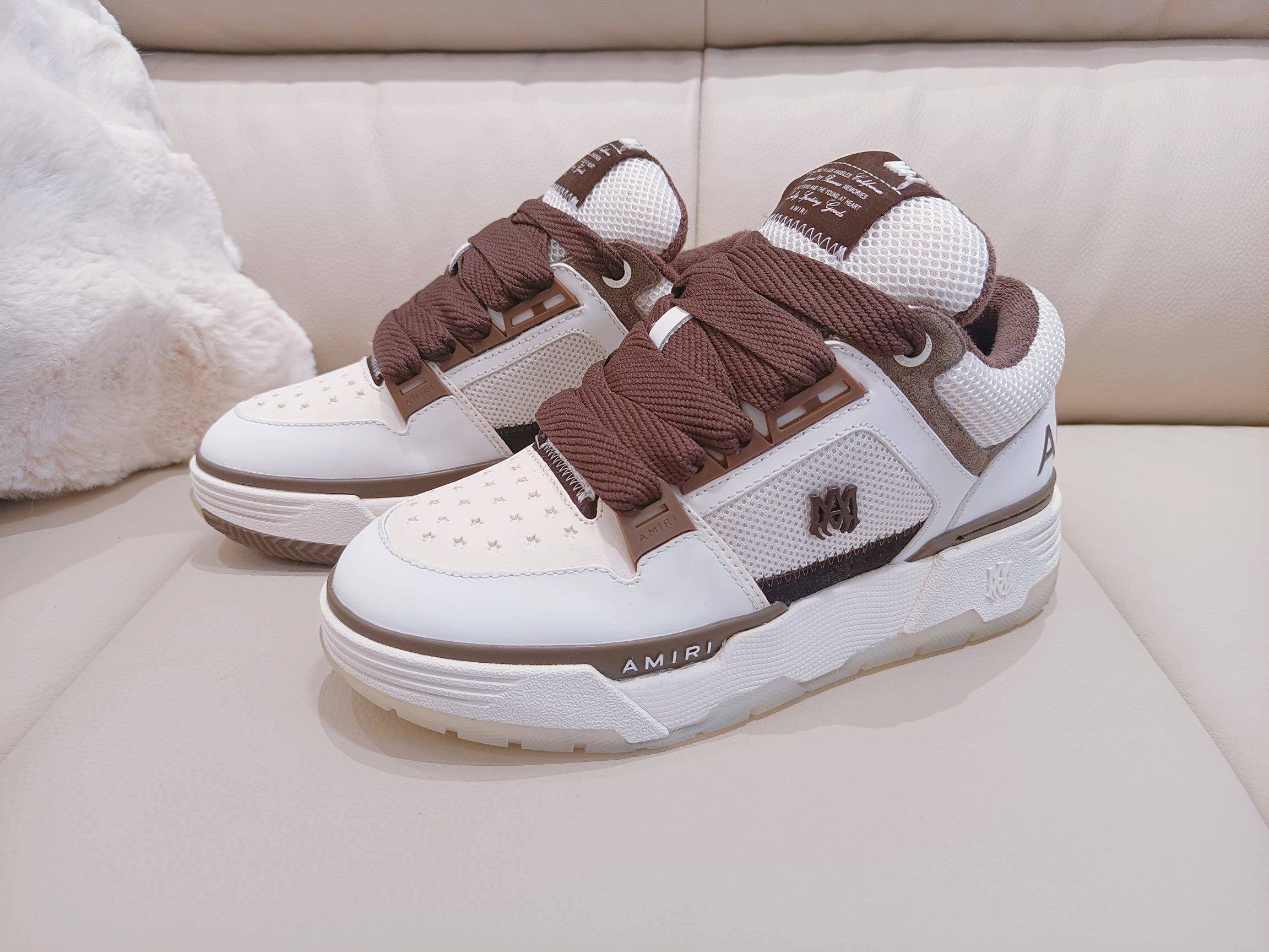 White low-top sneakers with brown laces and side logo patch, lace-up front