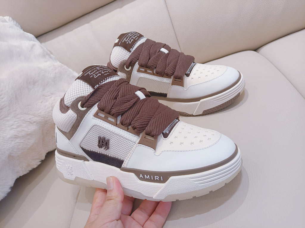 White low-top sneakers with brown laces, held by hand near the front