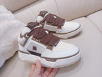 White low-top sneakers with brown laces, held by hand near the front
