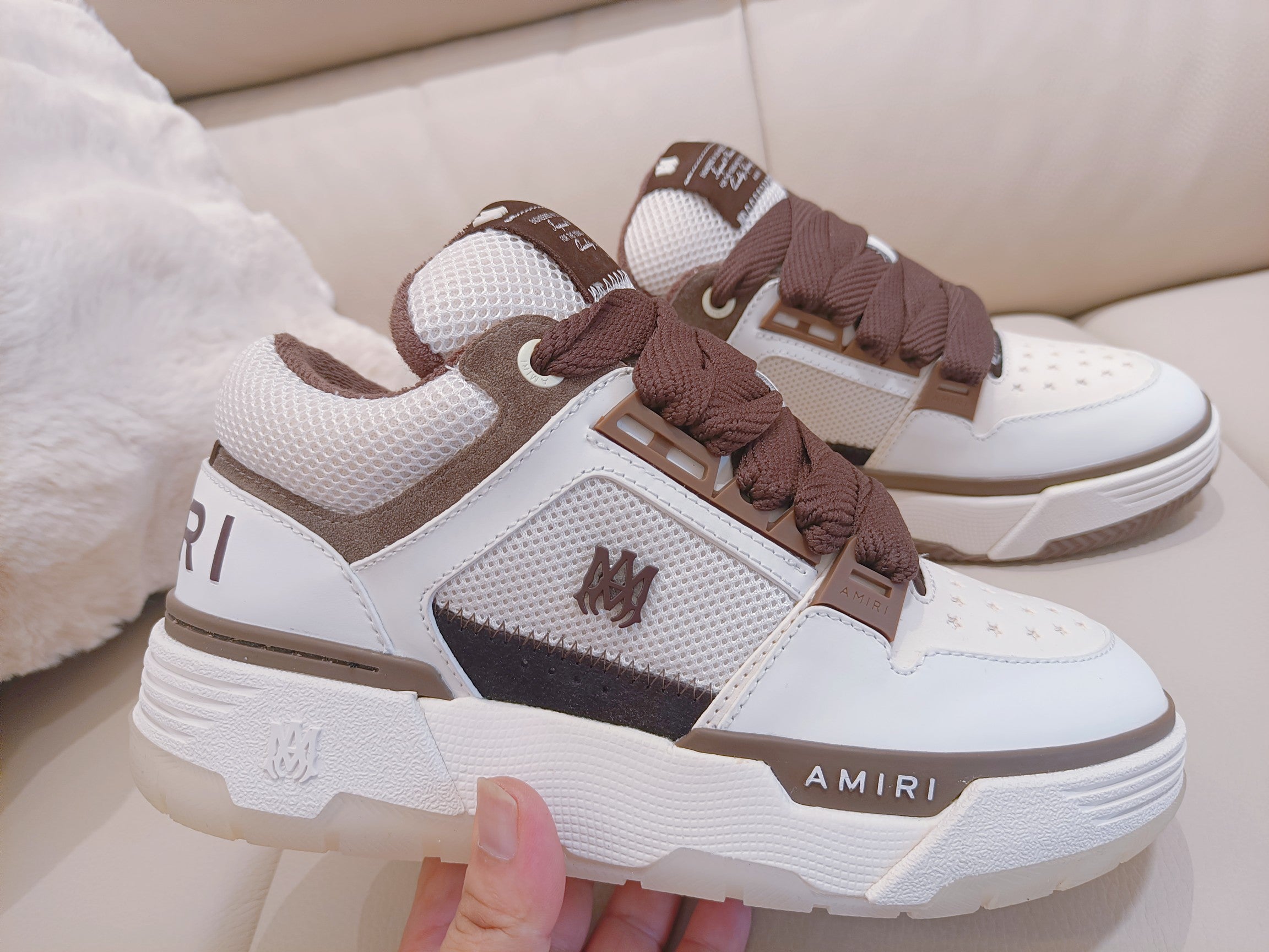 White low-top sneakers with brown laces, mesh panels, and AMIRI branding