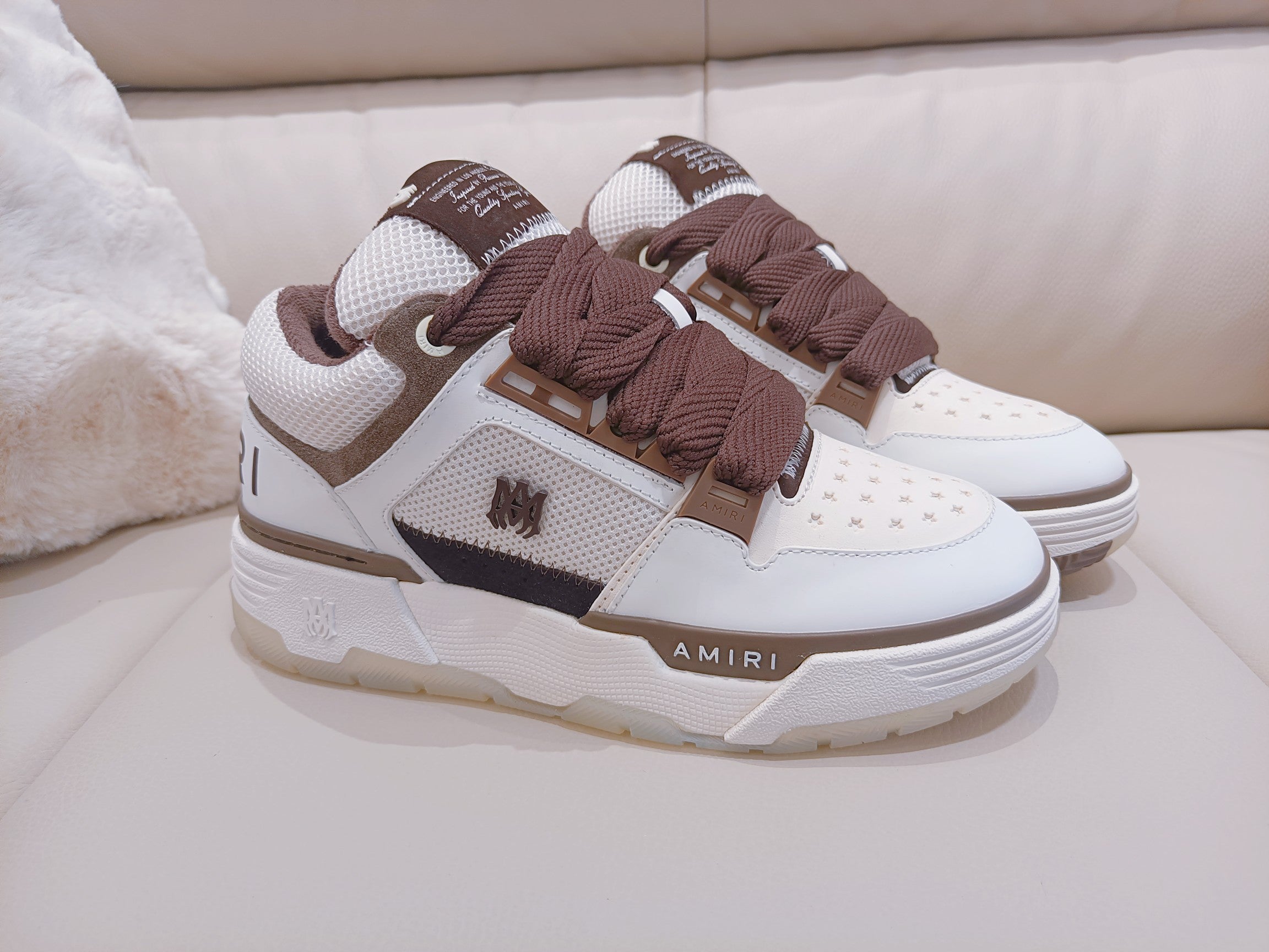 White low-top sneakers with brown laces and dark side stripe, logo accents