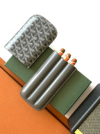 Small Goyard patterned bag with gray leather strap, holding three rolled items