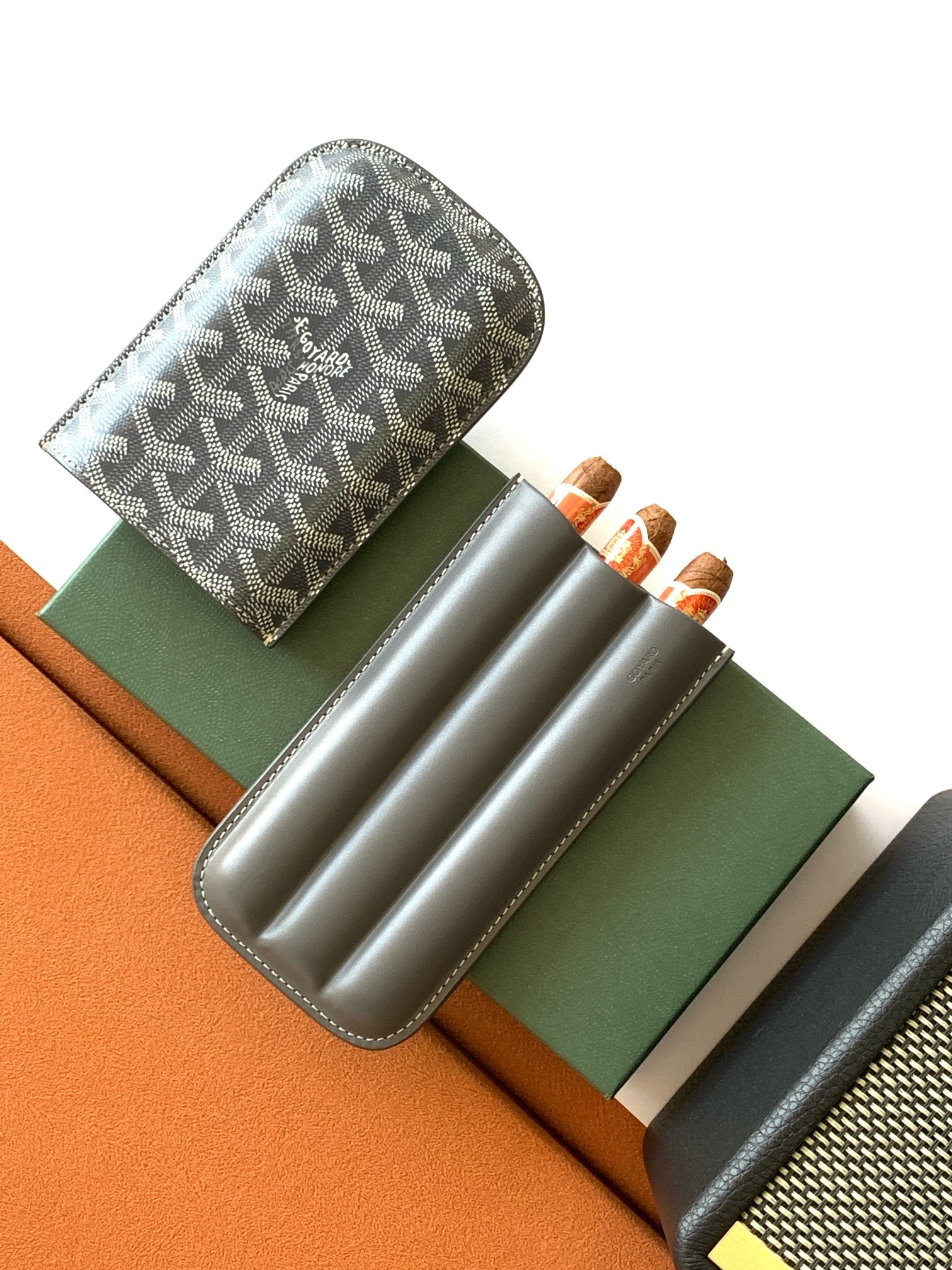 Small Goyard patterned bag with gray leather strap, holding three rolled items