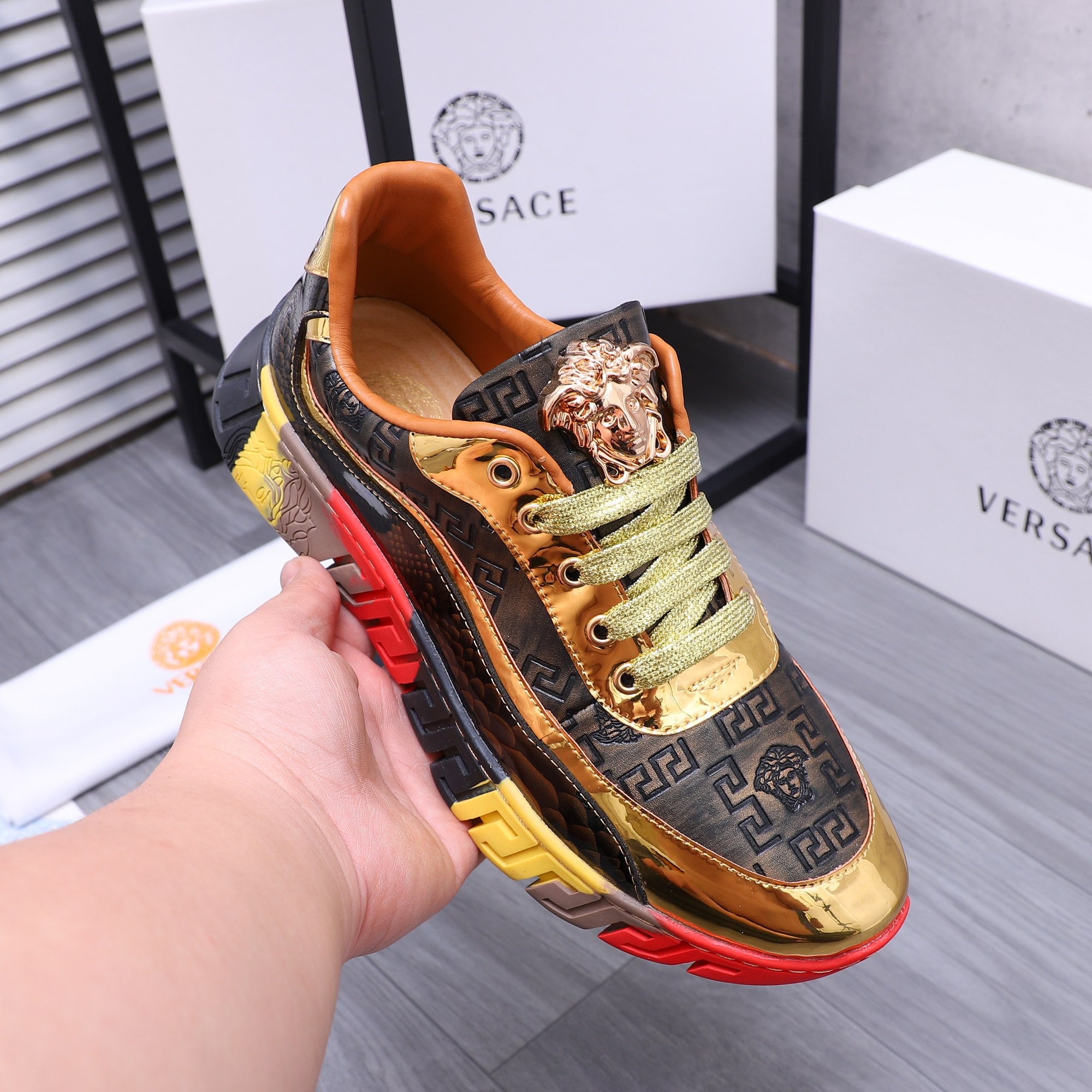 Luxury sneakers held in hand, gold Medusa emblem, navy upper, green laces, red/yellow sole