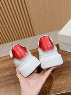 White sneakers with red back panels and cushioned heel tabs, held up.