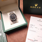 Rolex wristwatch in open box with black dial and silver-tone metal bracelet beside receipt