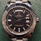Rolex Day-Date wristwatch close-up, black dial, fluted bezel, day-date markers at 12 and 3