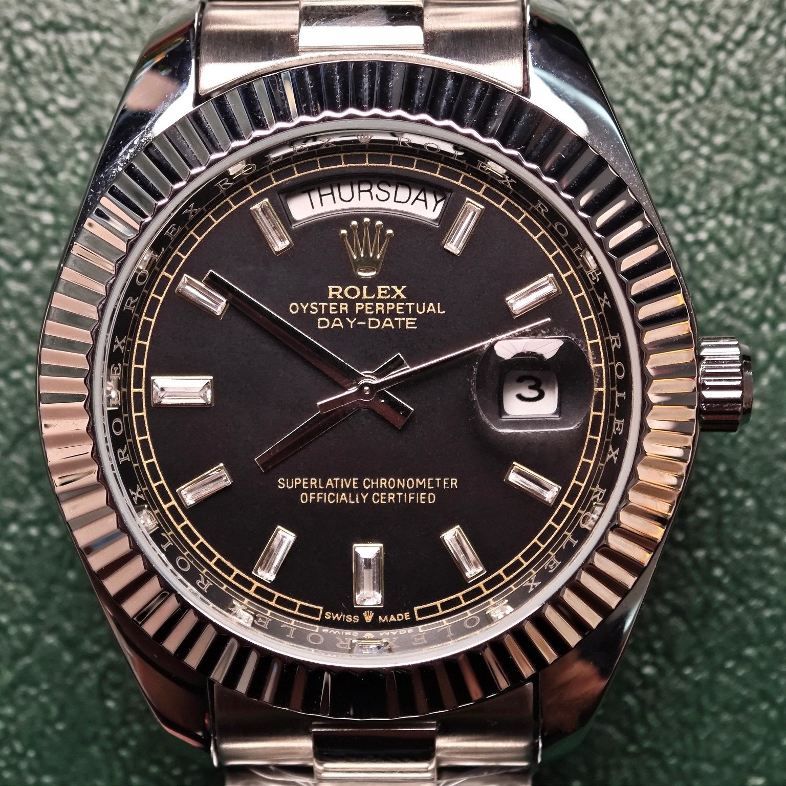 Rolex Day-Date wristwatch close-up, black dial, fluted bezel, day-date markers at 12 and 3