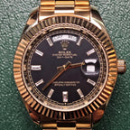 Gold-tone Rolex watch dial with 'DAY-DATE', black face, metal bracelet