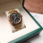 Rolex watch on display box, black dial, gold-tone metal bracelet