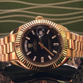 Gold-tone Rolex watch with black dial, date window, fluted bezel, metal bracelet