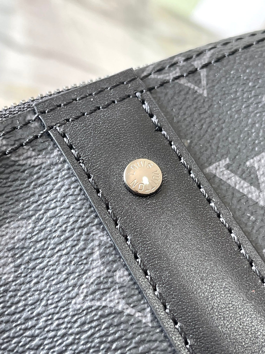Louis Vuitton bag corner detail with stitched leather panel and round logo rivet
