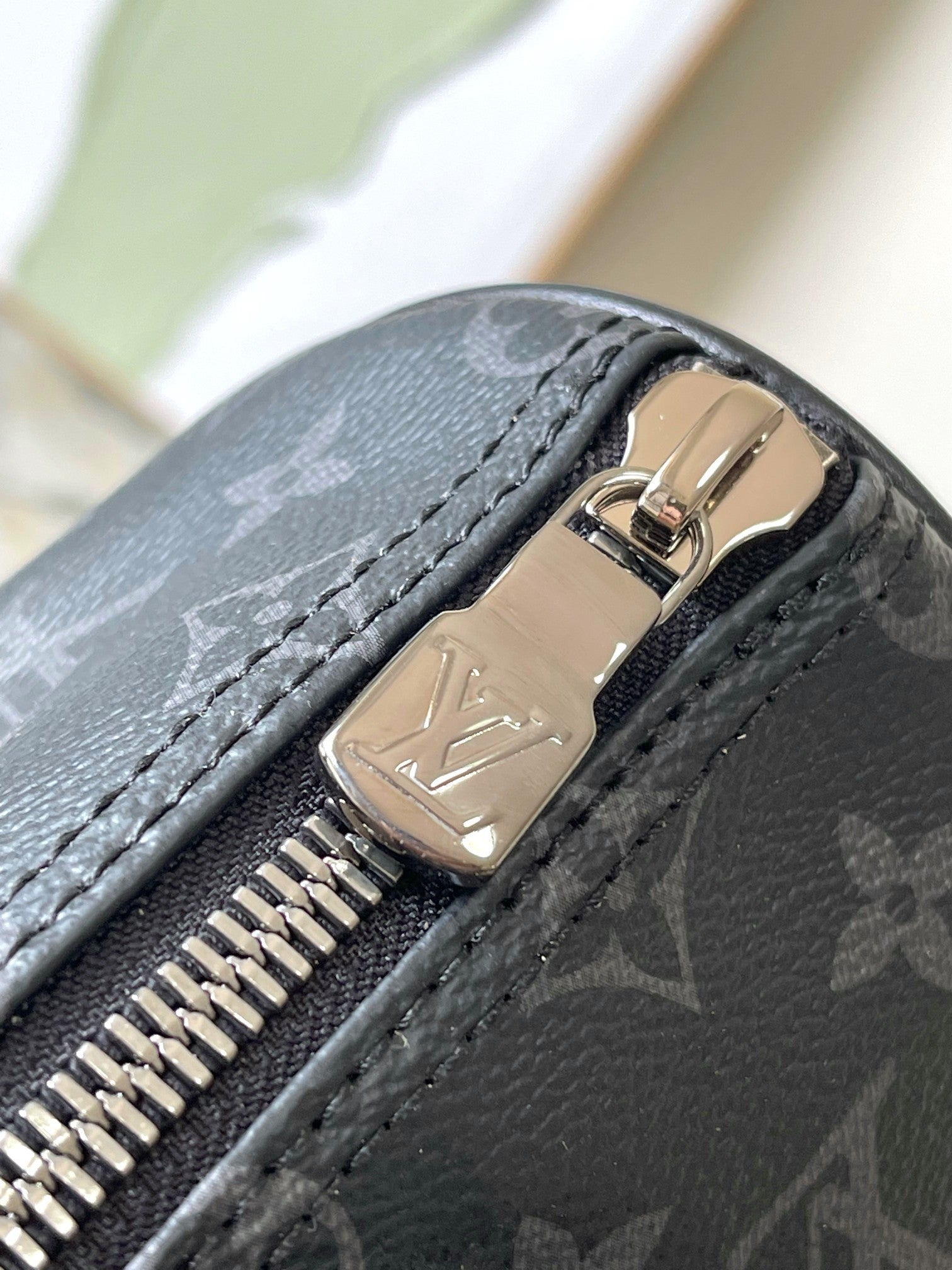 Louis Vuitton handbag zipper close-up with dark monogram leather and metal pull tab