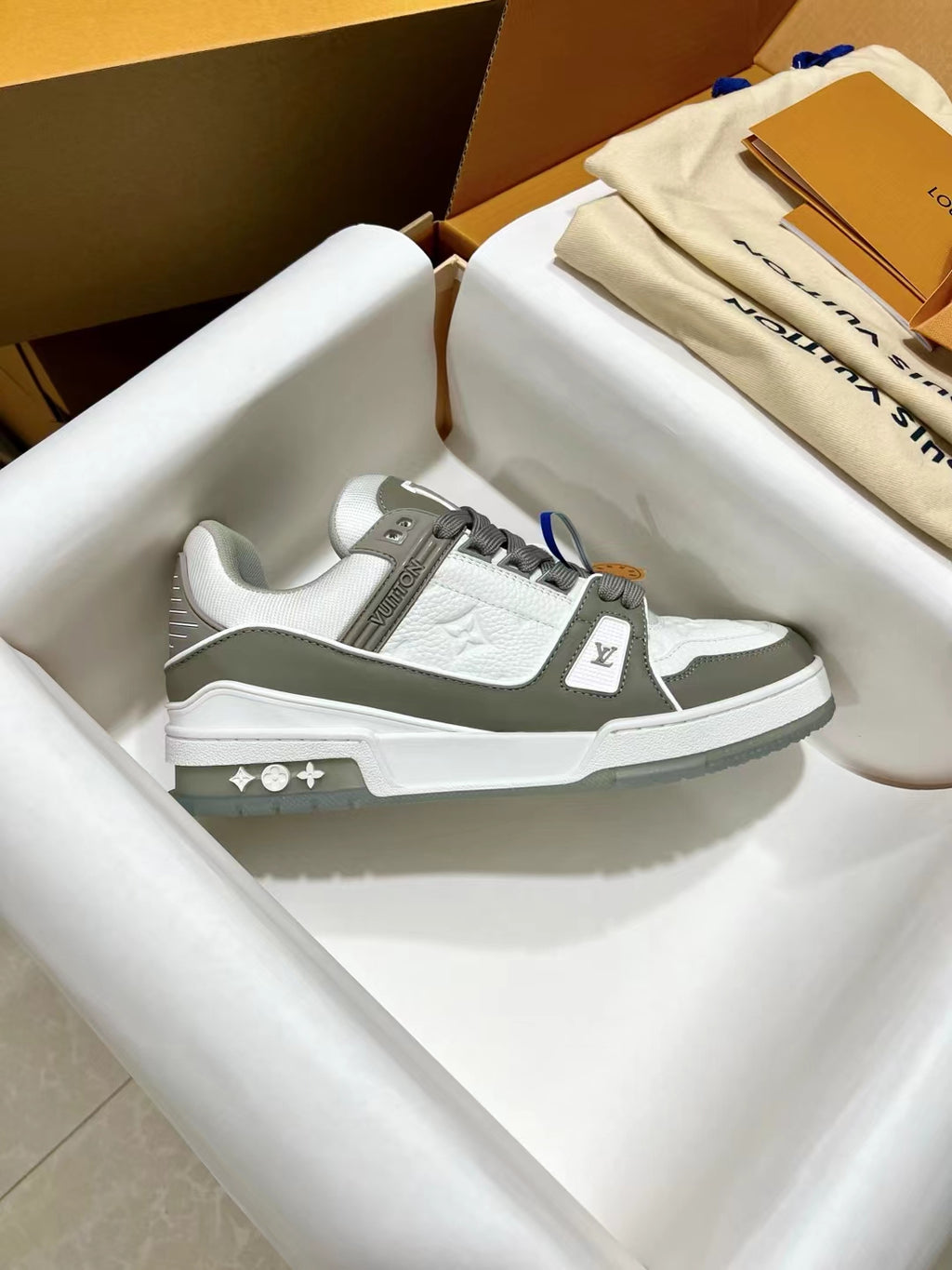 Louis Vuitton trainer sneakers, side view with white uppers, gray straps, LV emblem
