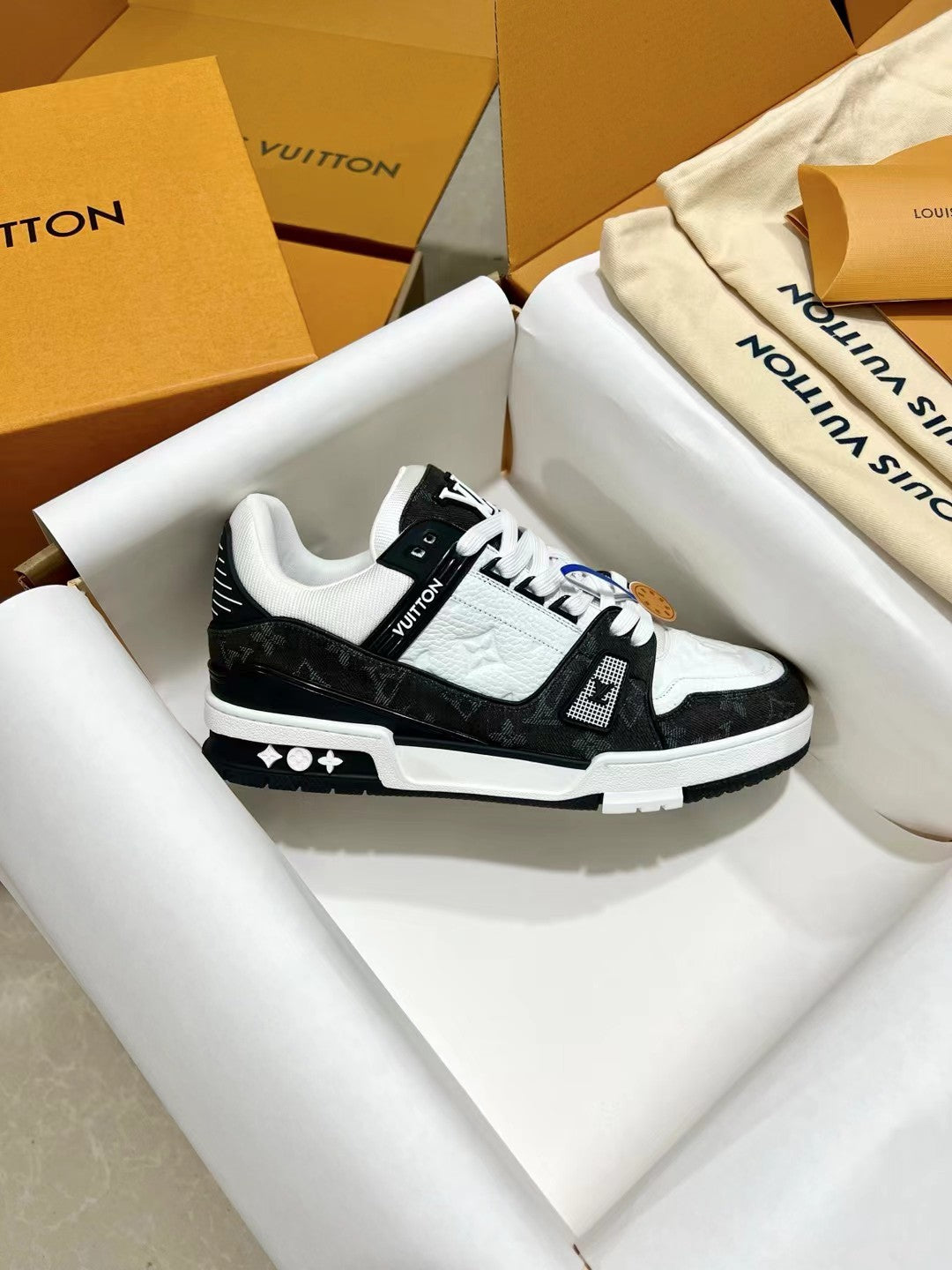 Low-top trainer sneakers side view, black and white uppers with LV logo badge