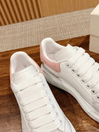 White low-top sneakers with pink suede heel panels and lace-up closure, pair