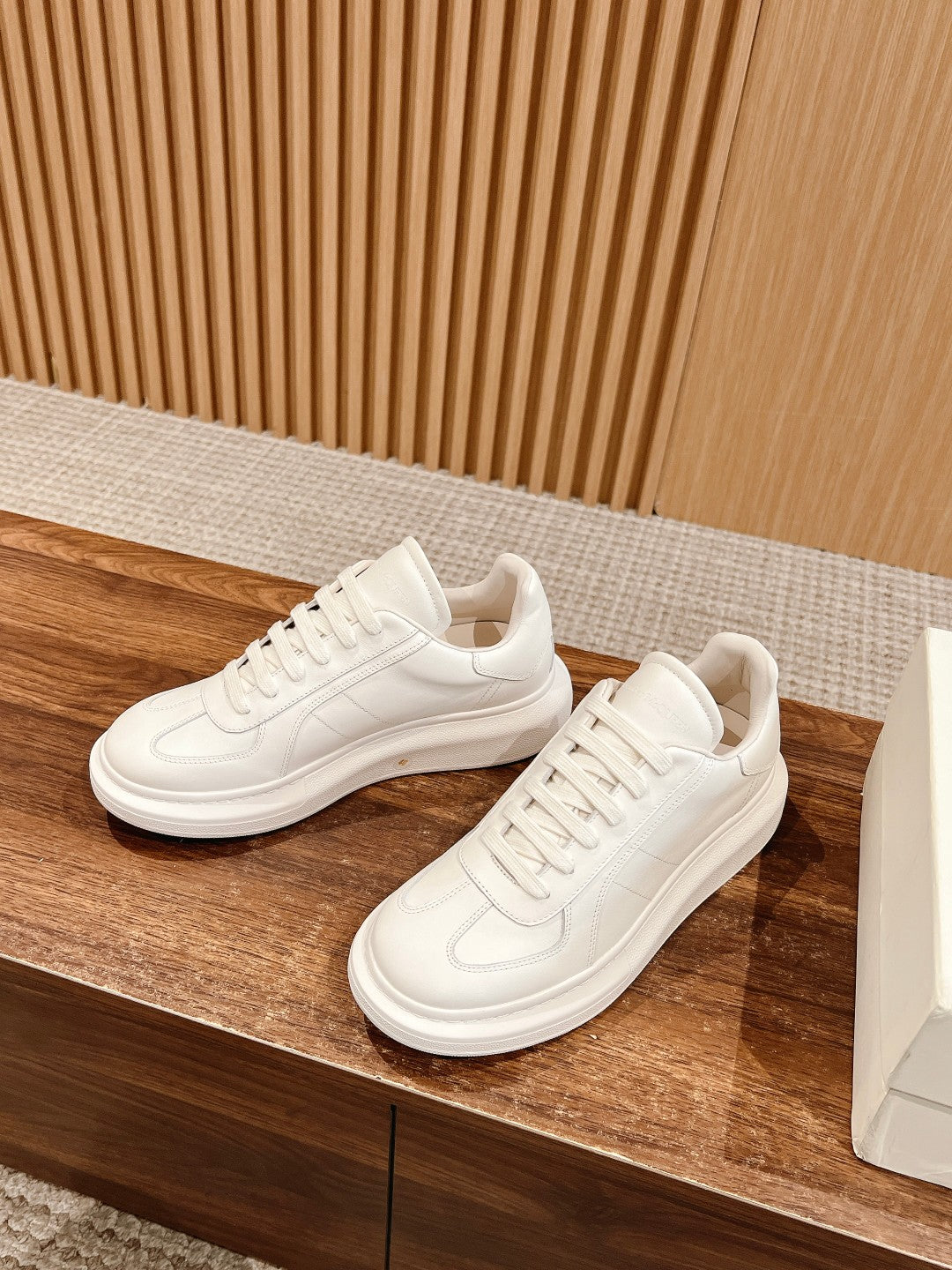 White lace-up sneakers pair on a wooden surface, side profile view