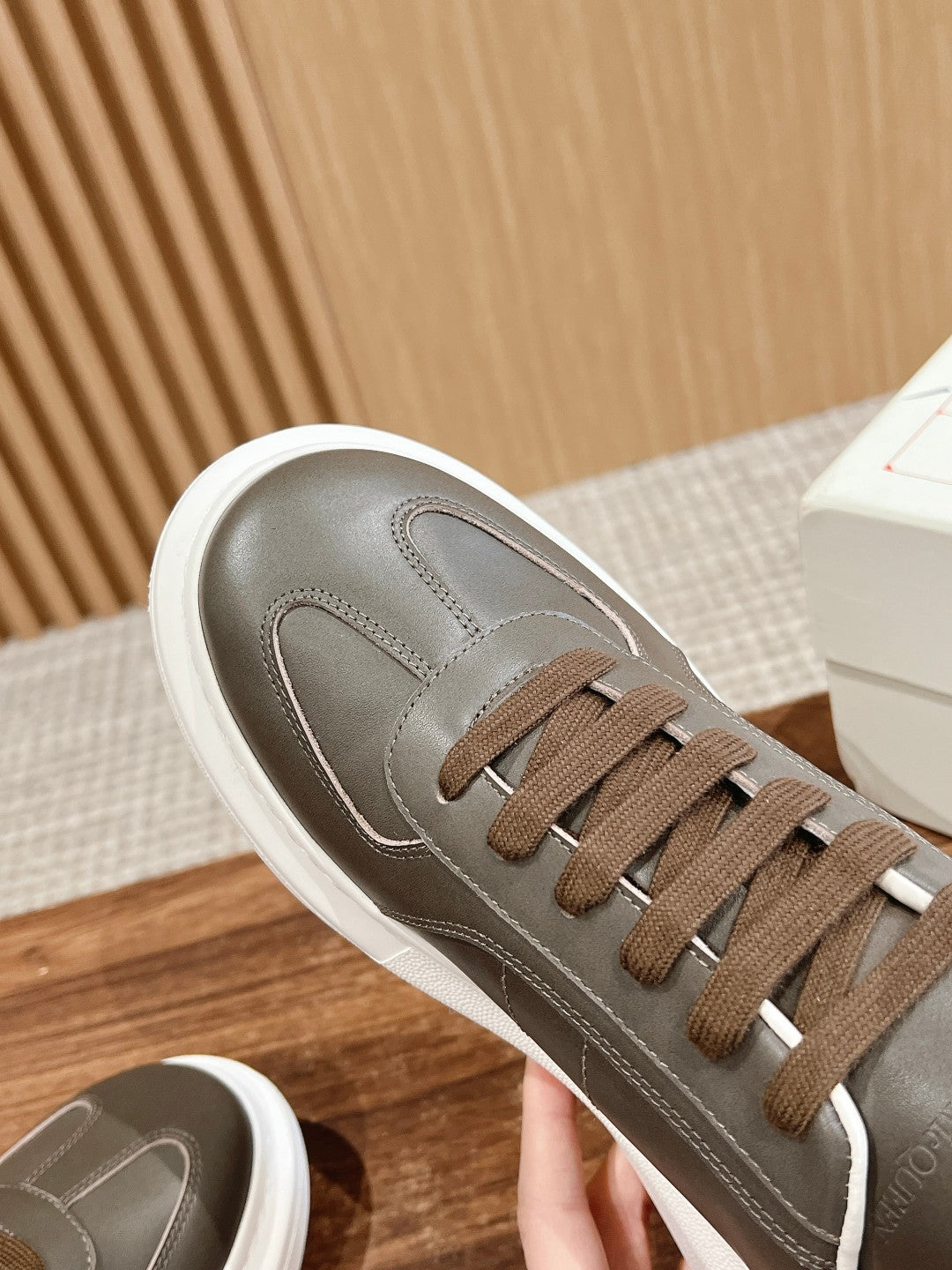 Side view of dark gray leather low-top sneaker with white sole and brown laces