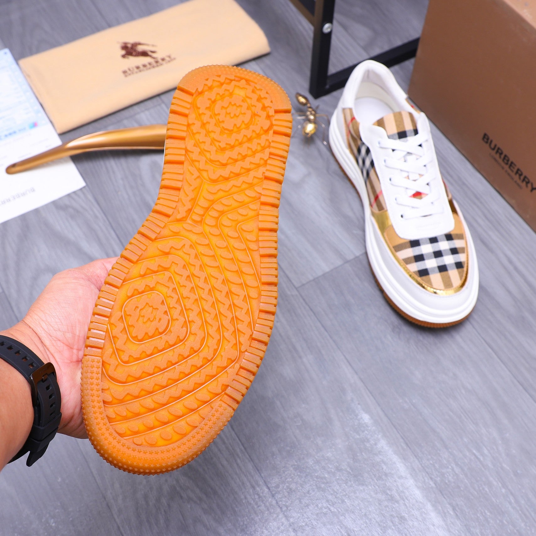 Orange rubber outsole tread of a Burberry sneaker with white check upper