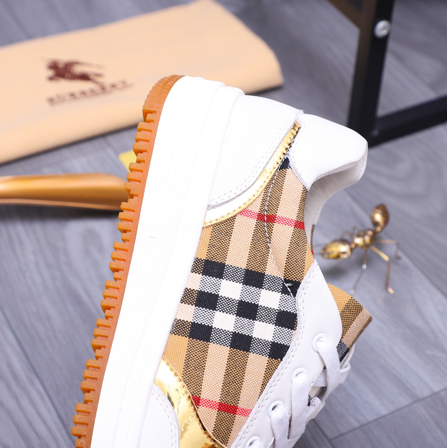 Side view of white Burberry sneaker with check panel upper and orange sole edge