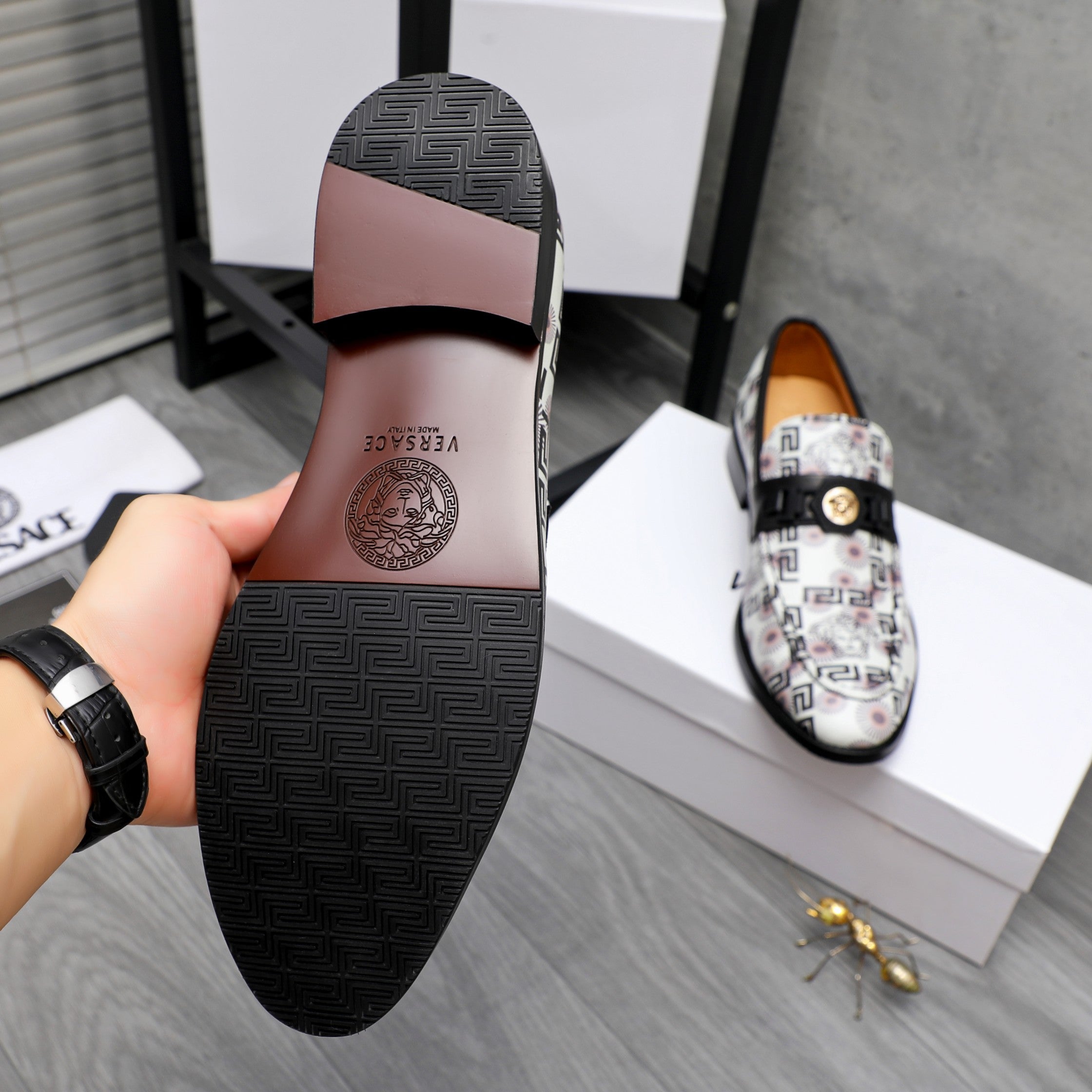 Versace loafer outsole with dark rubber tread and logo, viewed from heel side.