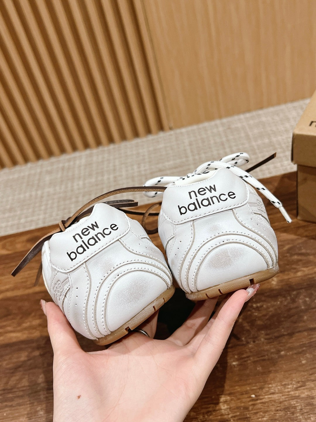 Pair of white low-top sneakers held in hands, showing New Balance heels