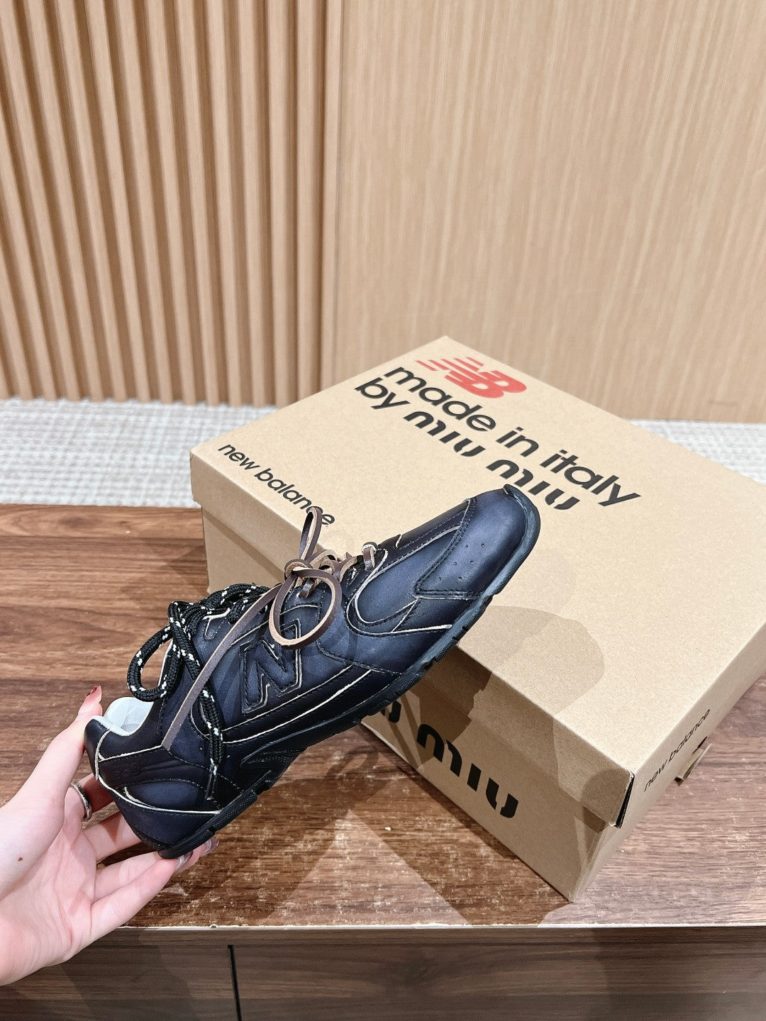 Black unisex sneakers with white laces and low-profile soles, hand-held
