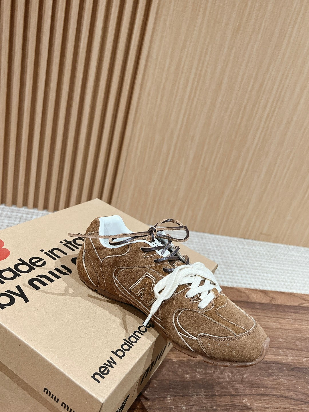 Pair of brown suede sneakers with white laces on box, side logo and lace tie.