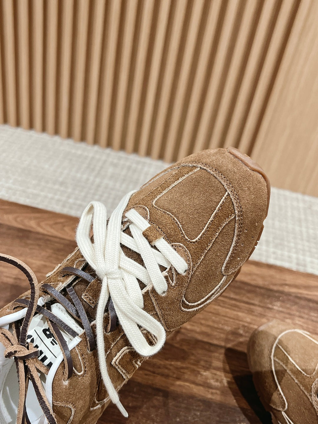 Brown suede sneaker with white laces, close-up of side seams and stitching.