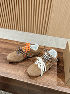 Brown suede sneakers with white laces and orange laces, side view, logo detail.