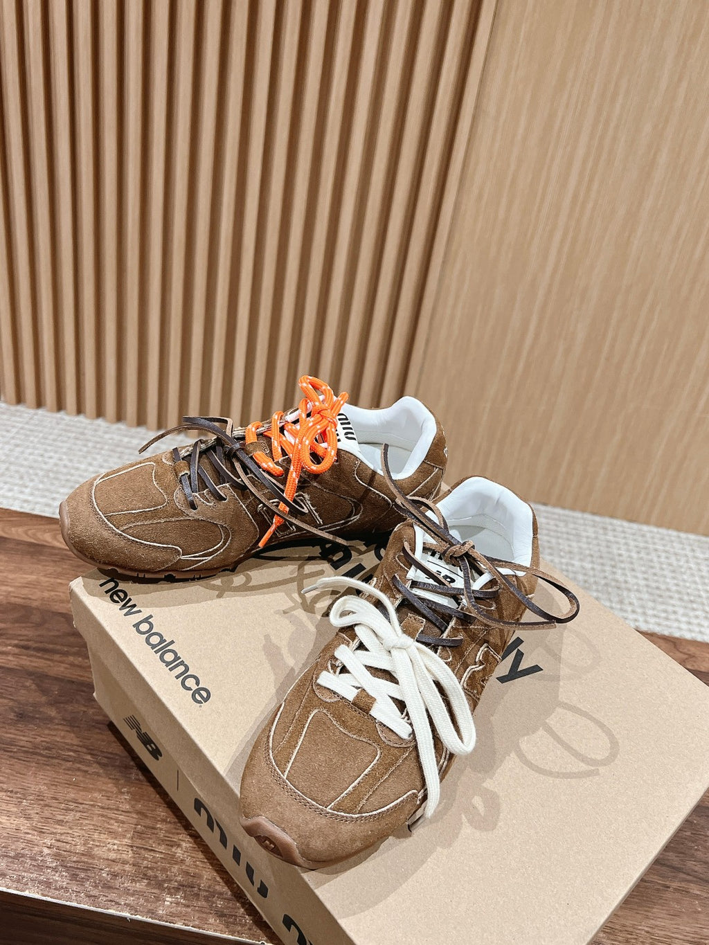 Brown suede sneakers with orange and black laces, white tongue detail, top angle.