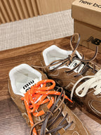 Brown suede sneakers with white and orange laces, white-lined tongue and lace tags.