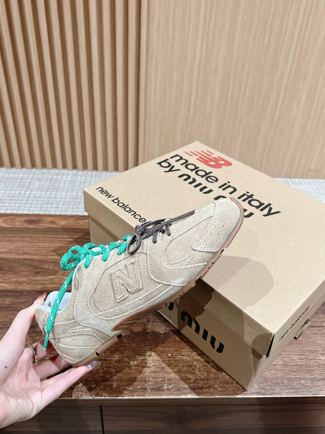 Unisex suede sneakers with green laces on brown shoebox; left shoe lifted