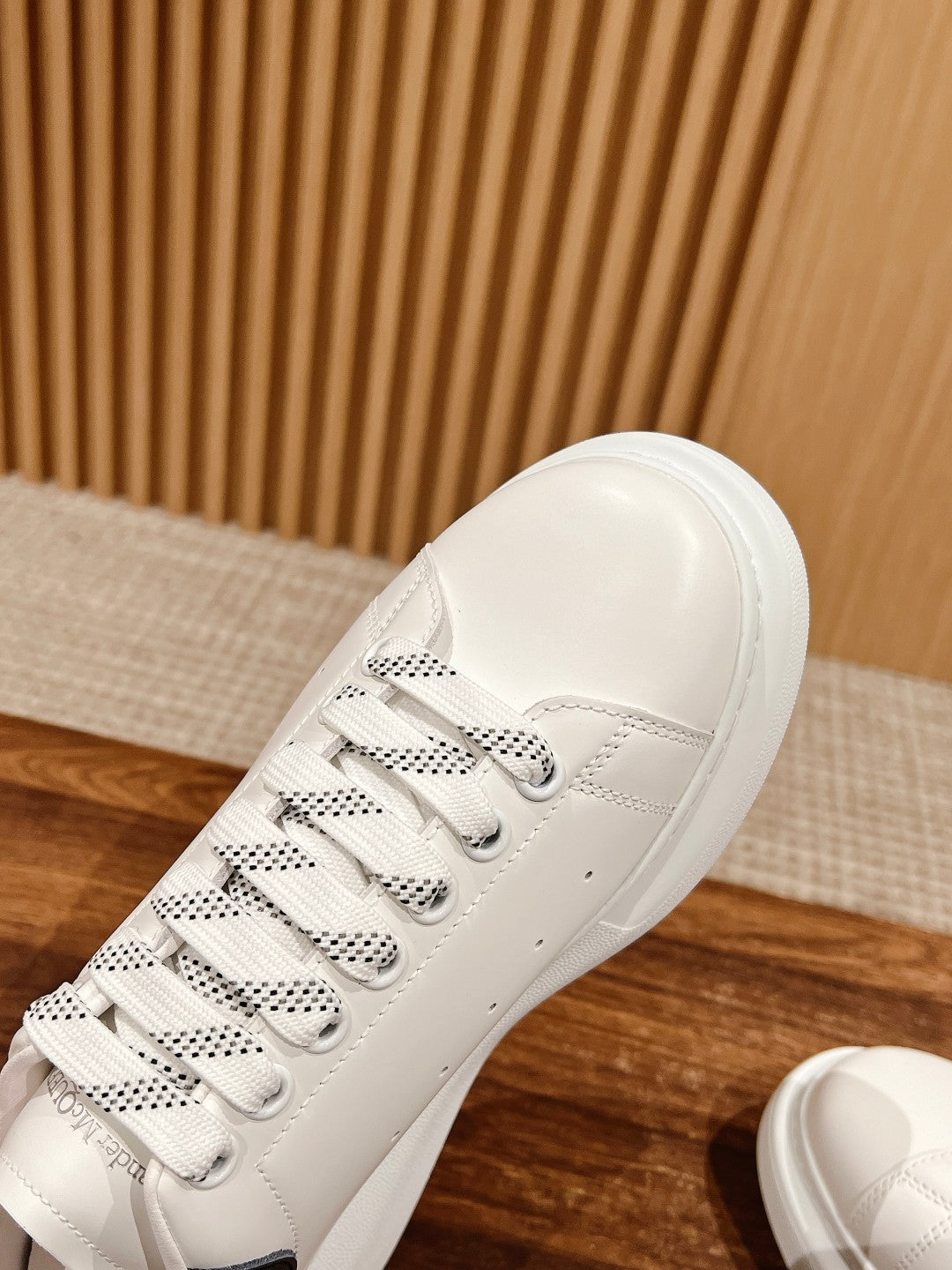 White leather sneaker close-up showing lace eyelets and navy heel accent