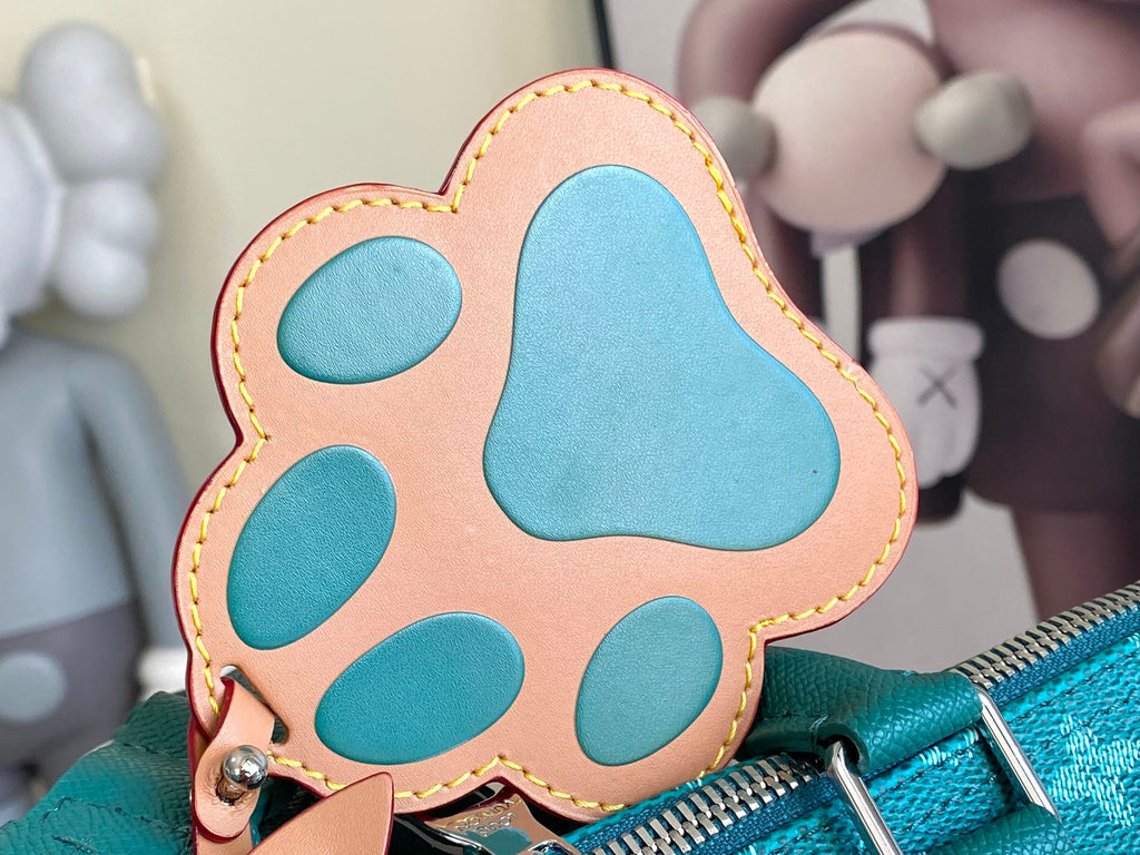 Teal and tan paw-shaped leather tag with gold-toned stitching and small metal ring