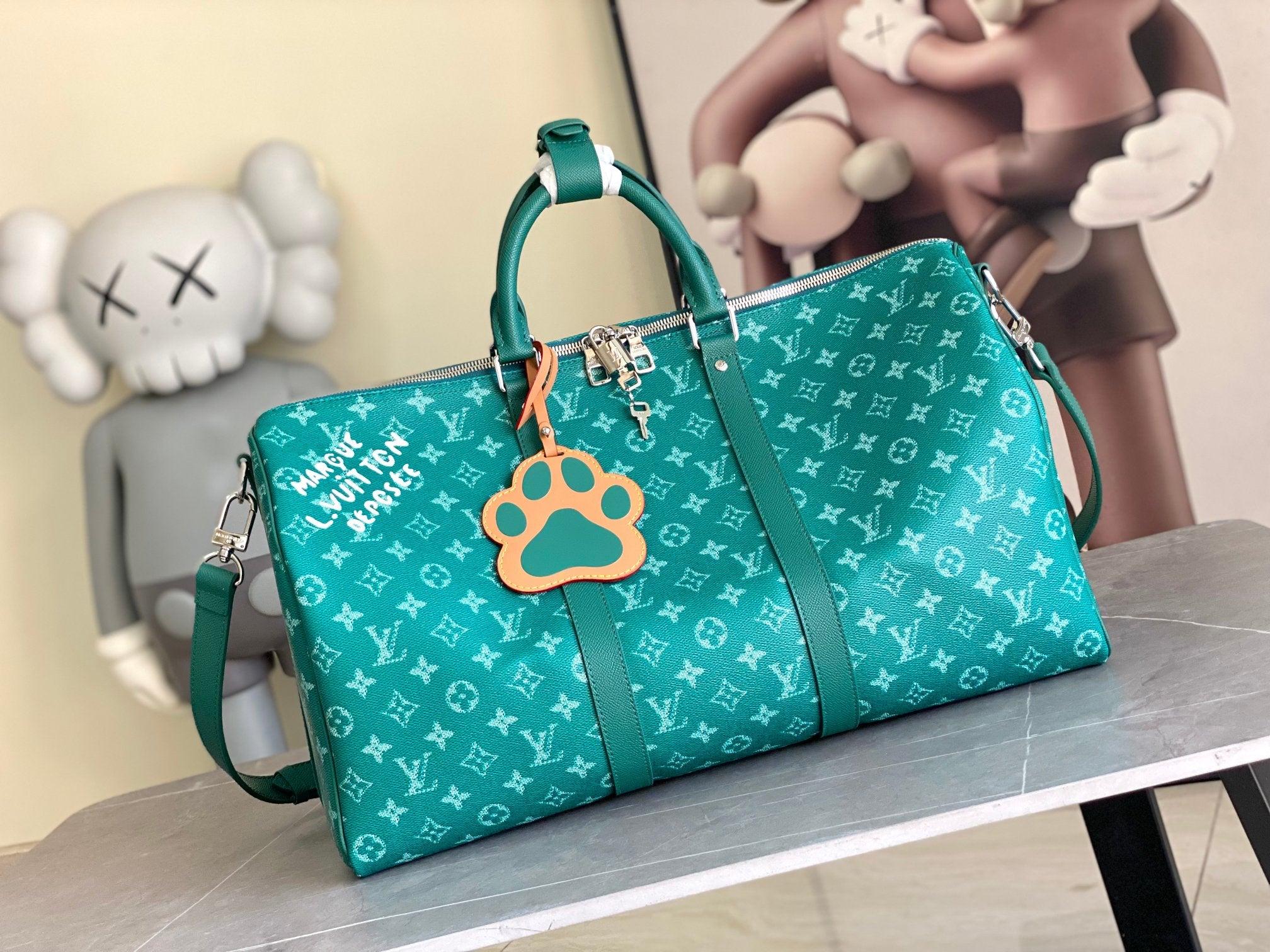 Teal monogram duffel bag with top handles, shoulder strap, and paw-shaped charm